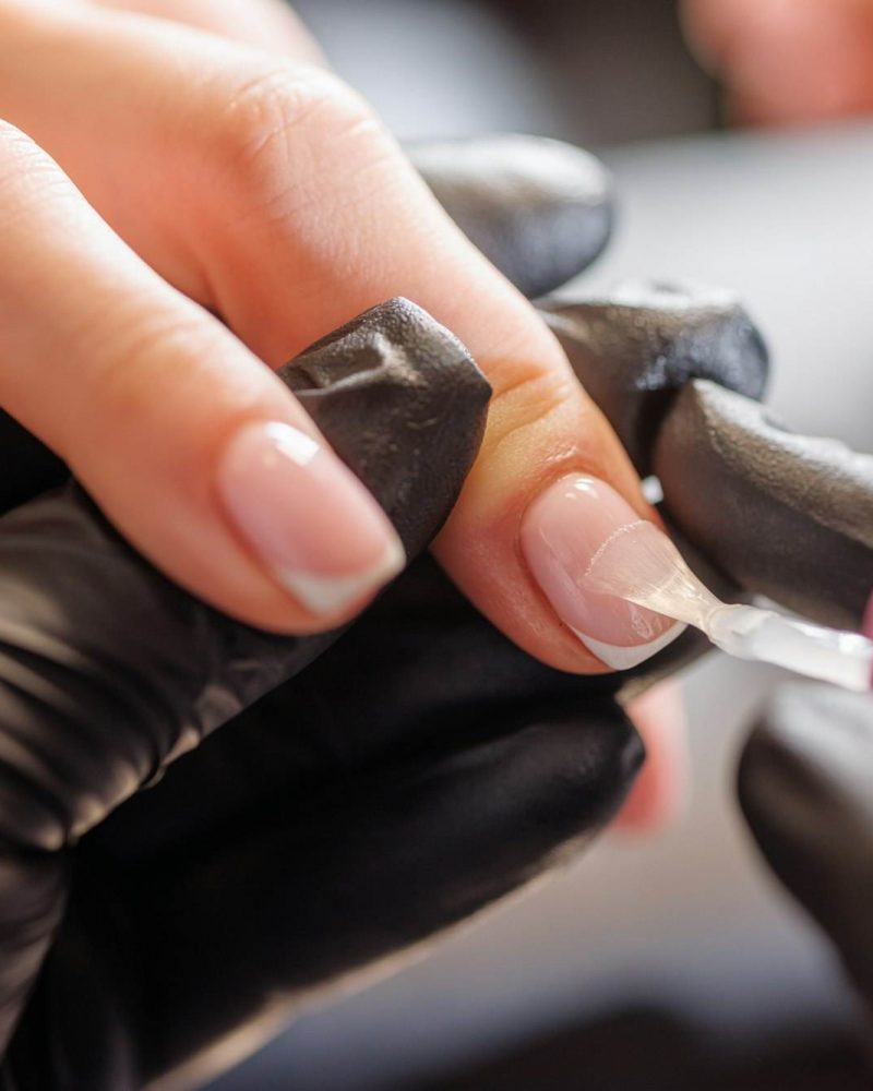 manicurist applies varnish to client's nails for hand care in beauty salon